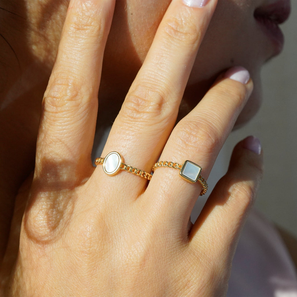 Close up of 18k gold oval mother of pearl ring worn on fingers