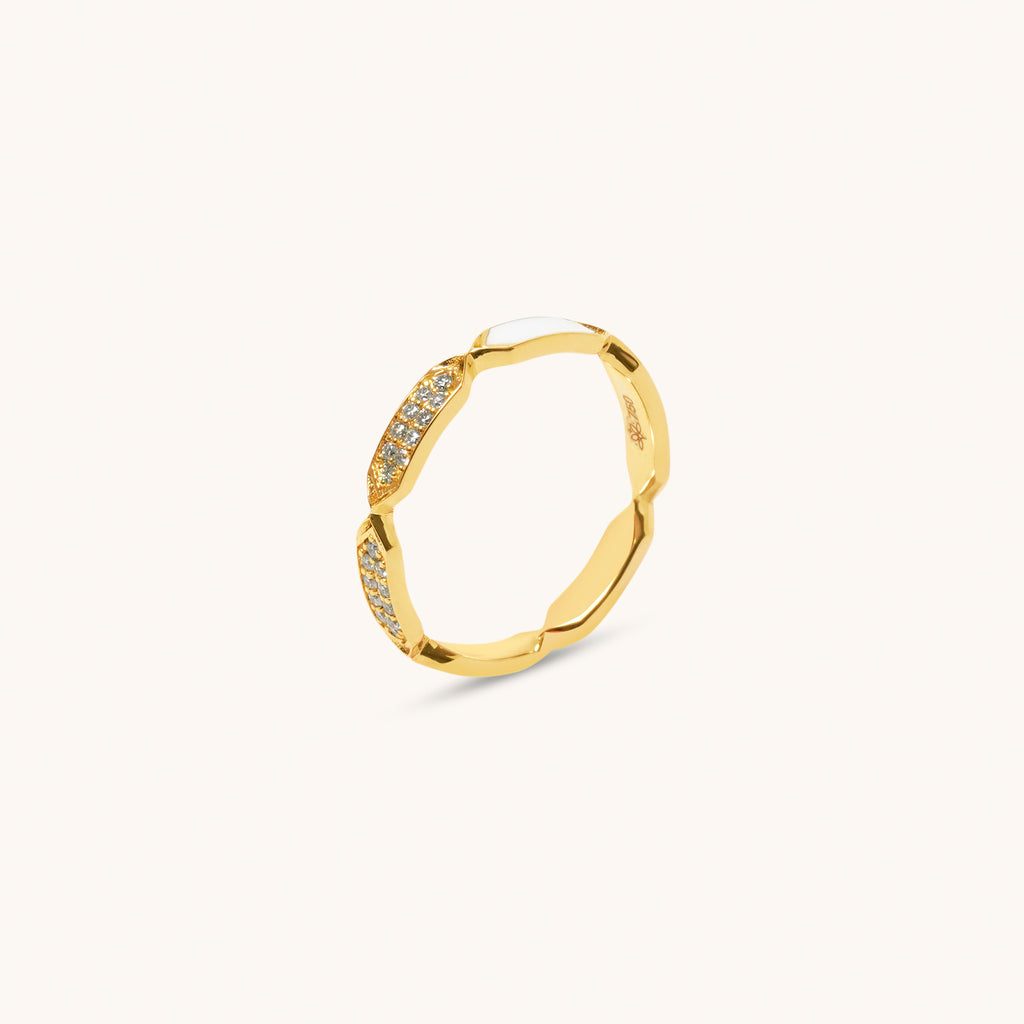 A gold ring with diamond facets and white enamel detailing, displayed against a white background