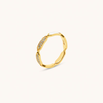 A gold ring with diamond facets and white enamel detailing, displayed against a white background