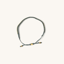 Load image into Gallery viewer, A top view of 18k gold bracelet for women with intertwined grey threads, featuring a fully adjustable design.