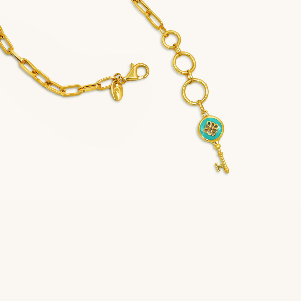Close-up of blue enamel key pendant and adjustable chain detail on 18K gold bracelet