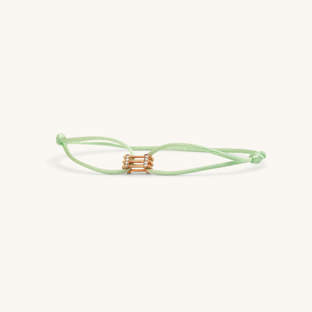 Flat lay of Kaleido Triad rose gold bracelet with pistachio green adjustable thread