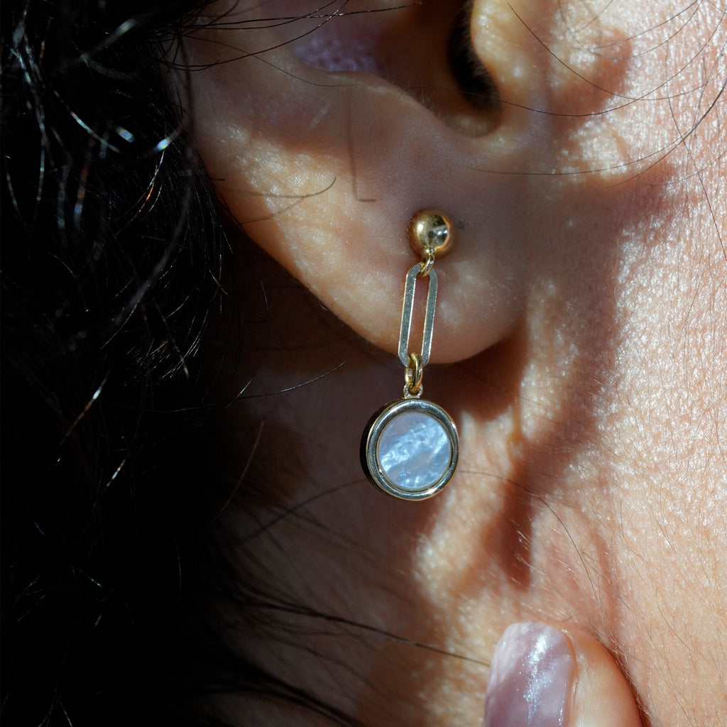 Close-up of woman wearing 18K gold mother-of-pearl drop earrings showing elegant dangling circular design